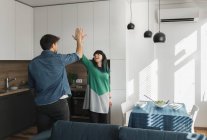 Fröhlicher junger Mann und Frau geben einander High Five, während sie gemeinsam in der modernen Küche stehen — Stockfoto