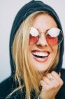 Young blond woman in sunglasses and hoodie laughing on white background — Stock Photo