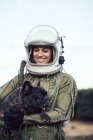 Усміхнена дівчина в старому космічному шоломі і скафандр тримає собаку в природі — стокове фото