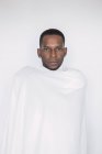 Портрет впевненого чорного чоловіка, загорнутого в білий аркуш на білому тлі — стокове фото