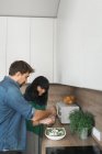 Side view of handsome young guy and lovely woman cooking healthy salad while standing in stylish kitchen together — Stock Photo
