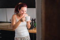 Сміється молода жінка п'є каву на кухні — стокове фото