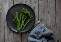 Steamed broccoli on black plate on wooden table — Stock Photo