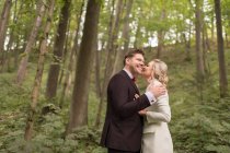 From above shot of embracing adult bride and groom standing in green woods — Stock Photo