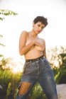 Fiduciosa donna provocante in denim in piedi in topless che copre il seno e guarda la fotocamera in natura — Foto stock