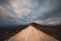 Row of modern windmills standing on side of narrow countryside road on cloudy day — Stock Photo