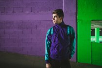 Jeune homme réfléchi en vêtements de sport debout contre un mur coloré — Photo de stock