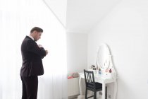 Вид збоку на молодого красивого чоловіка, що стоїть у білій спальні і одягає чорний офіційний костюм — стокове фото