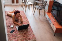 Jeune femme couchée sur le sol à la maison et utilisant un ordinateur portable — Photo de stock