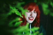 Crinkling young red haired woman between fir twigs on black background — Stock Photo