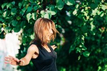 Femme élégante gaie debout sous l'arbre et souriant à la caméra dans le parc — Photo de stock