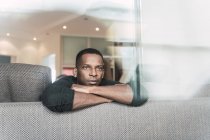Sonhando homem negro se apoiando em mãos enquanto sentado no sofá e olhando para longe — Fotografia de Stock
