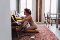 Молода жінка сидить на підлозі і використовує ноутбук вдома — стокове фото