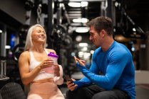 Cheerful fit man and woman sitting in gym and laughing — Stock Photo