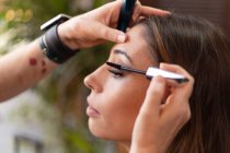 Hände eines unkenntlichen Make-up-Künstlers mit Pinsel, um schwarze Mascara auf die Wimpern der attraktiven Frau aufzutragen — Stockfoto