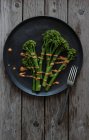 Пару брокколі з соусом ромашка на чорній тарілці з виделкою на дерев'яному столі — стокове фото