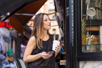 Femme avec boisson et smartphone près d'un café extérieur — Photo de stock