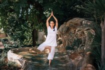 Жінка стоїть у фонтанній воді в позі дерева під час виконання йоги в парку — стокове фото