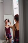 Giovane donna sorridente che tocca i capelli davanti allo specchio — Foto stock
