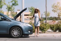 Chica de pie delante de su coche roto - foto de stock