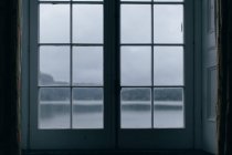 Lac calme entouré de montagnes sous un ciel dégagé à travers une fenêtre fermée — Photo de stock
