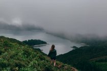 Женщина, стоящая на высоком холме с озером внизу — стоковое фото