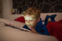 Усміхнений маленький хлопчик дивиться мультфільми з цифровим планшетом у ліжку — стокове фото
