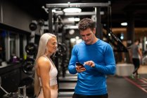 Спортивні чоловік і жінка за допомогою смартфона в тренажерний зал — стокове фото