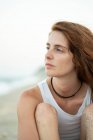 Beautiful young woman with ginger hair looking away while standing on blurred background of beach and sea in Tyulenovo, Bulgaria — Stock Photo