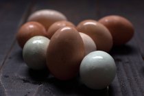Weiße und braune Eier mit nasser Schale auf dunklem Holztisch — Stockfoto