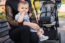 Porträt eines kleinen Mädchens, das im Freien auf dem Schoß der Mutter sitzt und Daumen lutscht — Stockfoto
