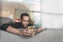 Africano homem americano usando smartphone no sofá em casa — Fotografia de Stock