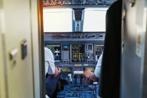 Control panel of cockpit with displays and indicators and two pilots in uniform navigating a plane — Stock Photo