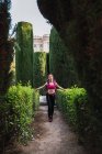 Sportswoman with pink backpack walking in park between lush green bushes at daylight — Stock Photo