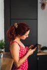 Усміхнена молода жінка в червоному однотонному купальнику стоїть в кімнаті і використовує мобільний телефон — стокове фото