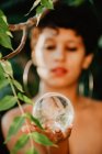 Молода топлес брюнетка жінка тримає скляний прозорий м'яч у зеленому лісі — стокове фото
