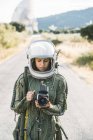 Дівчина в старому космічному шоломі і скафандр тримає фотоапарат на відкритому повітрі — стокове фото