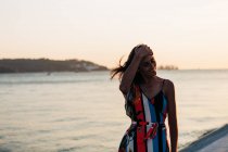 Rire jeune femme en robe d'été colorée debout sur la promenade au coucher du soleil — Photo de stock
