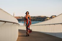 Elegant woman in long dress walking on bridge in summer city — Stock Photo