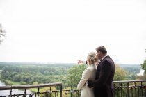 Rückansicht der Umarmung elegante Braut und Bräutigam stehen auf der Terrasse mit Vorhängeschlössern am Zaun und die Erkundung der Natur Ansichten — Stockfoto
