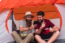 Путешественники едят и около палатки со смартфоном — стоковое фото