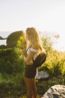 Vue latérale d'une femme méconnaissable en tenue décontractée debout près de la mer lors d'un coucher de soleil incroyable sur la plage en Californie — Photo de stock