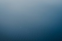 Повітряний вид на спокійне блакитне море і далекий плаваючий маленький білий човен — стокове фото