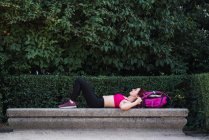 Спортсменка лежит на каменной скамейке в парке с рюкзаком — стоковое фото