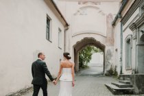 Vista posteriore del giovane uomo e dello sposo che si tengono per mano mentre camminano sulla bella strada della città vecchia — Foto stock