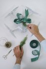 Чоловічі руки прикрашають загорнутий безпілотник як різдвяний подарунок з ялиновою гілкою та зеленою стрічкою на білому тлі — стокове фото