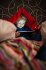 Sorridente bambino in pigiama utilizzando tablet digitale sotto coperta — Foto stock