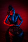 Jovem homem rastafarian africano gosta de ensaiar e joga tam tam tam, iluminação colorida vermelho e azul — Fotografia de Stock