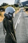 Female astronaut in helmet and spacesuit standing on road in countryside — Stock Photo