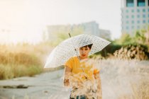Retrato de mujer joven con paraguas de pie bajo gotas de agua de pulverización - foto de stock